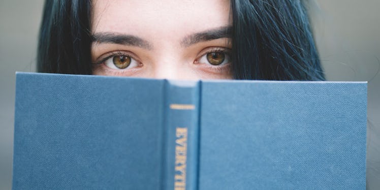 A dark haired woman peeking behind the book.