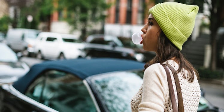 A woman with a lime hoodie walking down a street while blowing a bubble with her chewing gum, which ...
