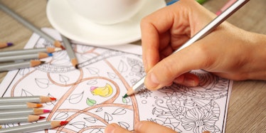 A closeup of a hand coloring in a coloring book to de-stress