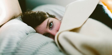 A woman peeking through a blanket while lying in bed.