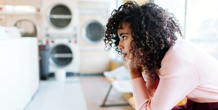 A curly haired woman sitting in laundry room.