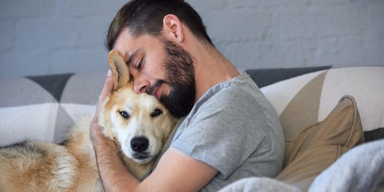 A man in a grey shirt sitting on a couch and hugging his dog, which apparently is stressing his dog ...