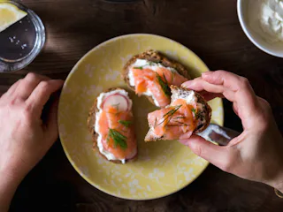 A person taking one of three salmon toast sandwiches from a yellow plate, which can boost your mood
