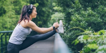 A woman stretching her legs on a bridge and listening to a song on headphones