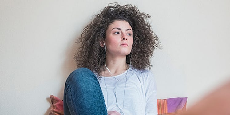 A curly-haired woman in a grey top and blue denim jeans sitting to manage anxiety and stress