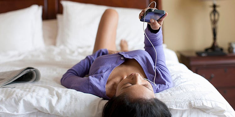 A woman in a blue sweater lying in her bed while holding her phone and looking for apps to conquer s...