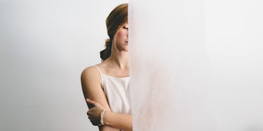 A stressed-out woman standing behind a white curtain.