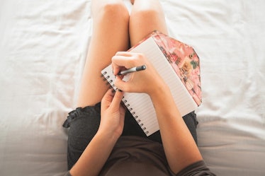 A woman lying in bed and writing on her notebook that is on her lap to manage anxiety and stress