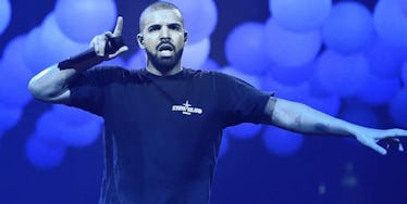 Drake on stage pointing upwards with his index finger while holding a microphone