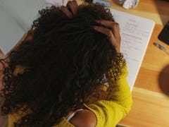 A curly-haired woman in a yellow sweater looking at her notebook during Virgo season