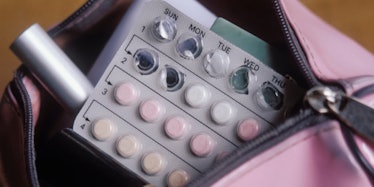 A pack of birth control pills peaking out of a makeup bag