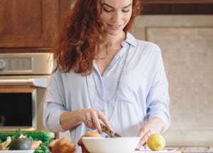 A ginger-haired girl on a plant-based diet cutting up vegetables in the kitchen.