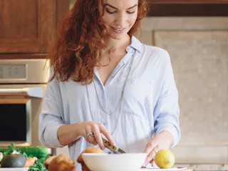 A ginger-haired girl on a plant-based diet cutting up vegetables in the kitchen.