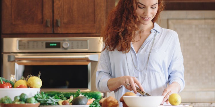 A ginger-haired girl on a plant-based diet cutting up vegetables in the kitchen.