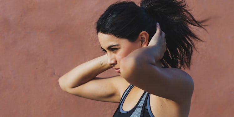 A young woman in running gear fixing her hair during a run.
