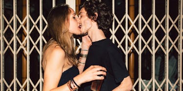 A dark-haired man and a brunette woman, both in black tops kissing in front of an elevator on their ...