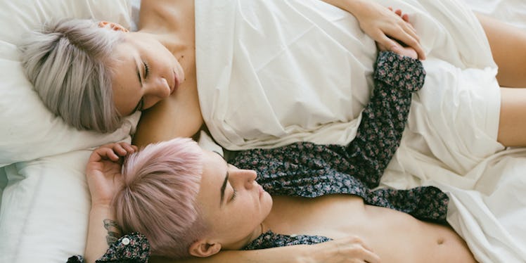 Two girls lying on the bed while holding hands.