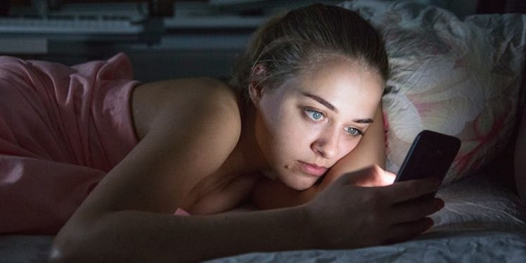 A young lady looking at her phone while in bed
