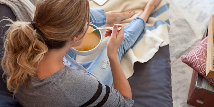 A woman sitting on a couch and eating soup