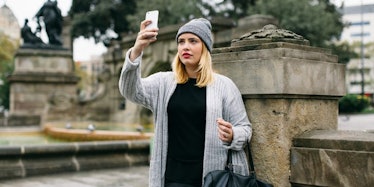 A woman standing alone looks at her phone.