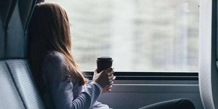 A woman on a train, holding a coffee cup and looking out the window as she deals with her mood being...
