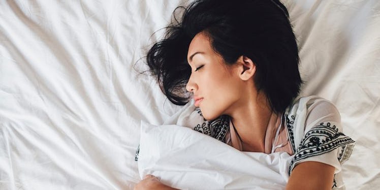 A dark haired woman stretching while lying in bed.