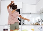 a young woman dancing around her kitchen in shorts.