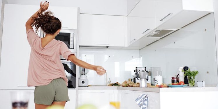 a young woman dancing around her kitchen in shorts.