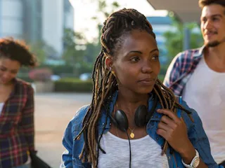 A girl in a white shirt, blue jacket and earphones experiencing back-to-school stress as she approac...