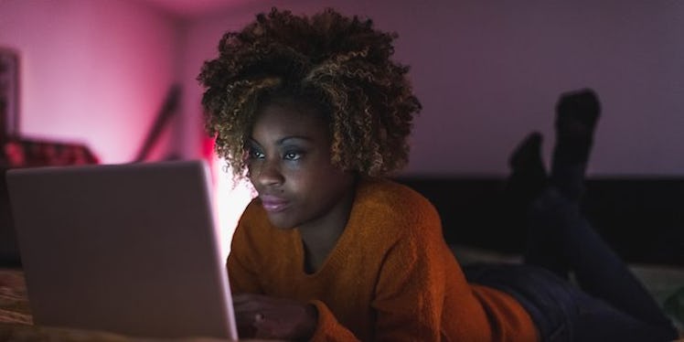 A girl with curly hair lying on the bed in the dark while browsing the best job for her Zodiac sign ...