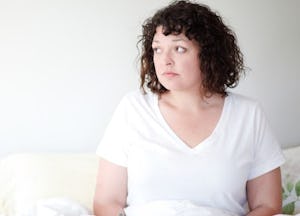 A woman with PCOS sitting on her couch, looking into the distance