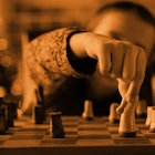 A child making a chess move while standing next to the chess set, pictured in sepia