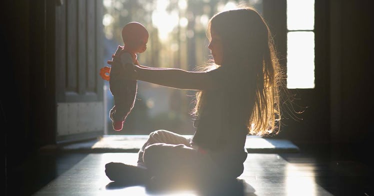A little girl sitting on the floor, holding a baby doll up in the air, while the sun shines upon her...