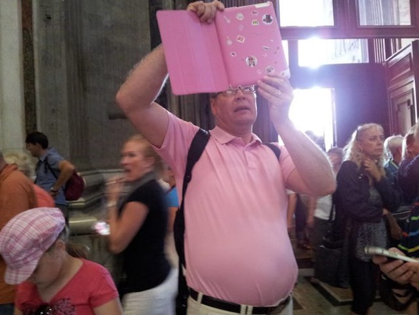 A dad in a pink shirt looking into a pink notebook in a crowded room