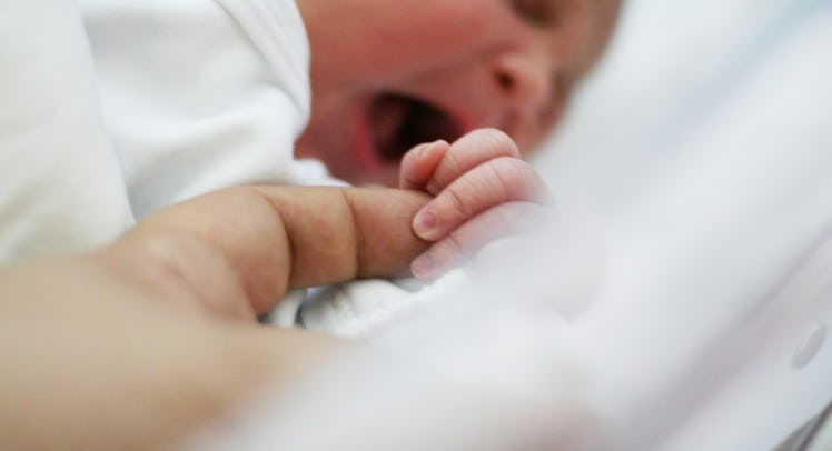 A newborn crying while holding a parent's finger