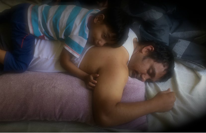 A young son leying on his dad's back while dad is sleeping