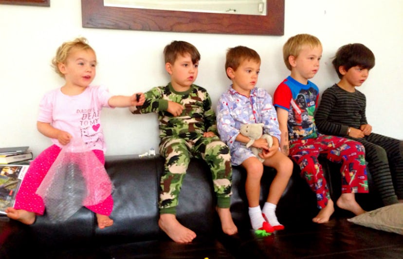 Five toddlers in their pajamas sitting on a leather pillow watching something in front of them