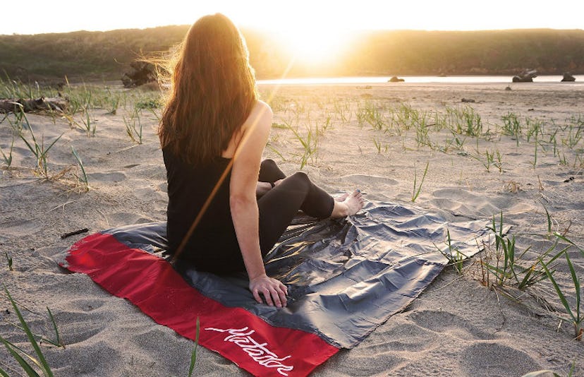 A woman watching the sunset on a beach while sitting on her Matador Pocket Blanket