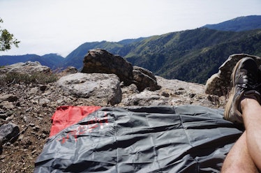 A man sitting on a blanket that fits in his pocket on top of a mountain site during the day
