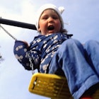 An extroverted toddler yelling while she swings on a swingset