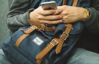 A person scrolling a phone with hands leaned on a backpack