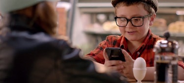 A digitally savvy kid in a diner using his phone but who also has limited screen time wearing glasse...