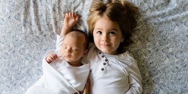 A little girl and her baby sibling lying on a bed while the baby is sleeping