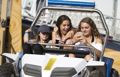 Three digitally savvy girls driving in a buggy and one of them is using her smartphone