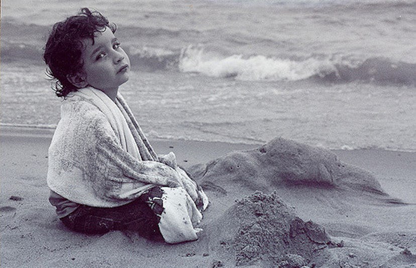 A young boy sitting alone on a sand beach