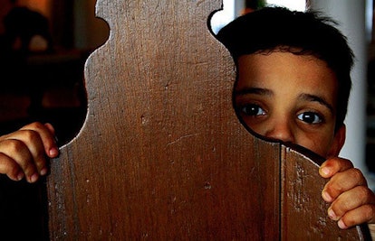 A young boy scared hiding behind a wooden object
