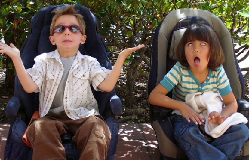 Two kids making exaggerated faces while sitting on car seats that are placed on the ground  