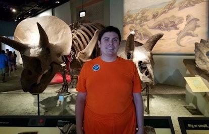 A father with severe autism posing for a photo in a museum with dinosaur skeletons behind him 