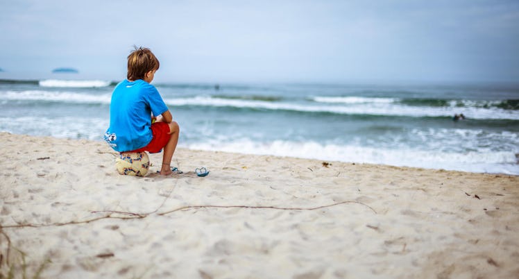 A little boy sitting on a ball at a sand beach