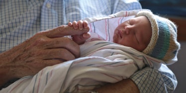 A newborn baby in a blanket holding her grandfather's index finger
